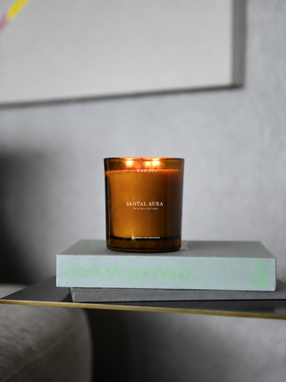 Vela Santal Aura 370 g de Madison en vidrio ámbar, encendida sobre libros de diseño.